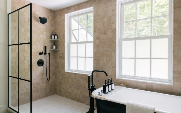 Primary bathroom with freestanding soaking tub, walk-in glass shower, and wood-grain tile walls illuminated by natural light from large windows